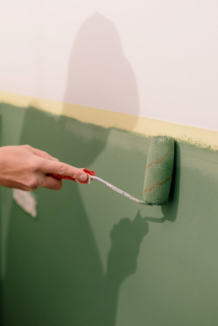 Crop anonymous person using roller brush with green paint and painting wall in apartment